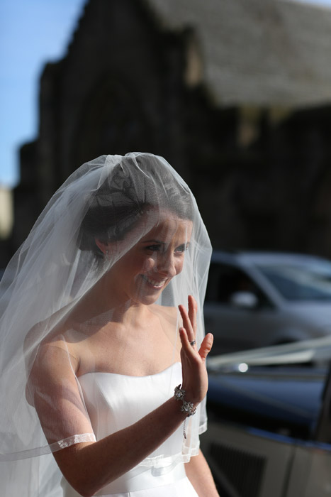 Photo of veiled bride smiling and waving in the sunshine