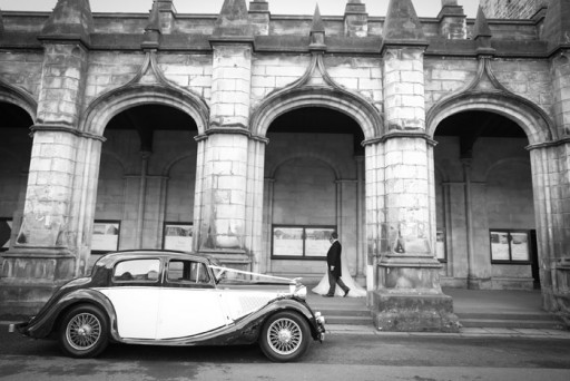 Photo of a vintage wedding car with bride and groom in background