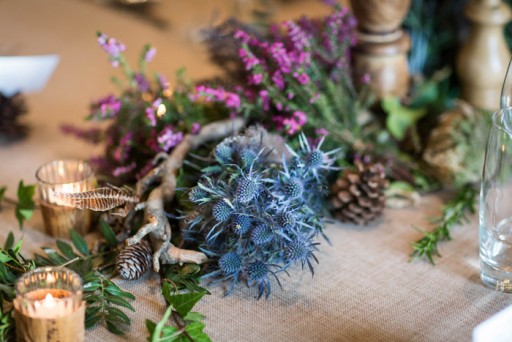 Photo of a Scottish wedding table flower arrangement with sea thistles, heather, rosemary and pine cones.