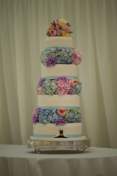 Photo of four tiered white wedding cake with flowers between each tier