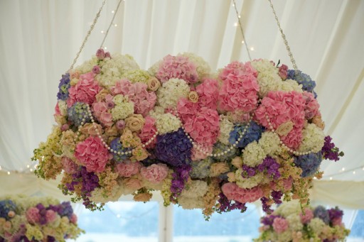 Photo of a cloud of cream, pink and lilac flowers with pearls suspended from the ceiling at a wedding reception