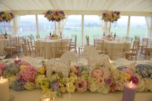Photo of marquee interior styled for a wedding reception with flowers and candles in pastel shades