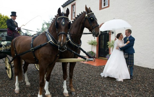 Photo of bride and groom standing next to their horse drawn carriage