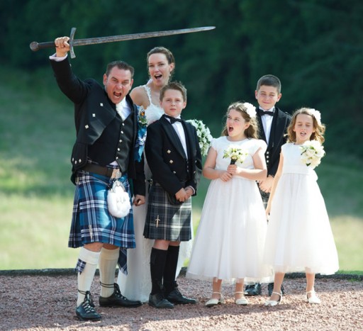 Photo of a groom at a Scottish wedding brandishing a sword while his bride, her flower girls and page boys cheer