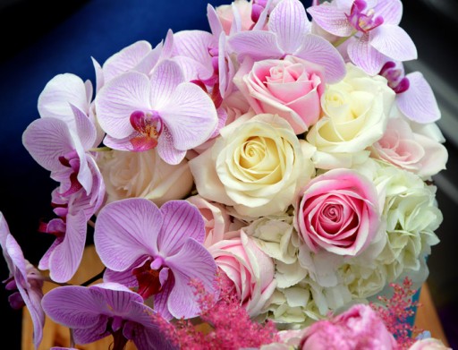 Close up photo of a wedding bouquet with ivory and pink roses and lilac orchids