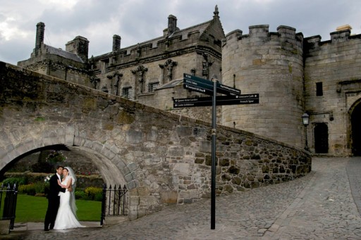 Photo of bride and groom embracing beneath arch in Scottish castle grounds