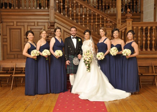 Photo of bride, groom and bridesmaids standing in front of a panelled wooden staircase