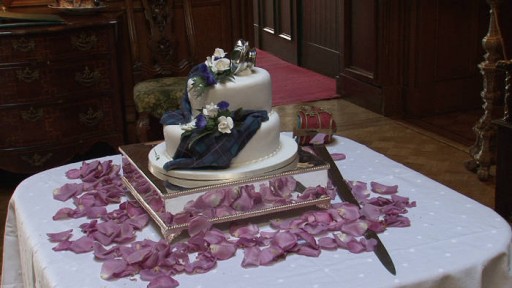 Two tier Scottish wedding cake with tartan decoration, flower petals and sword